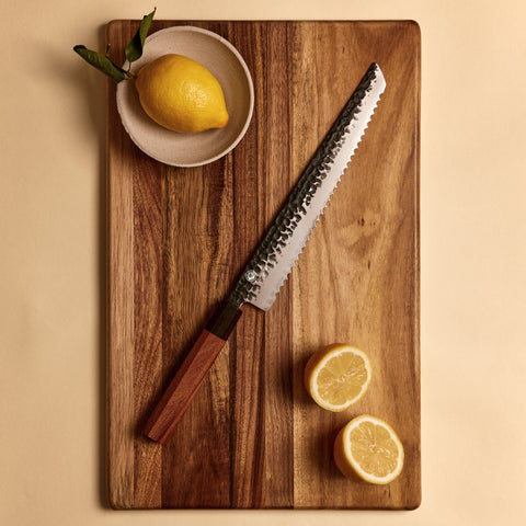 Yuzu Knives Japanese steel serrated bread knife on a walnut cutting board with lemons