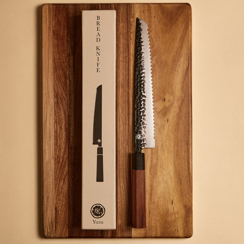 Bread knife next to its gift box packaging on a cutting board