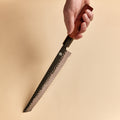 Hand holding a bread knife showing the serrated kurouchi blade