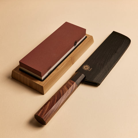 Nakiri knife in saya sheath next to dual-sided sharpening stone