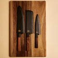 Three knives in wooden saya sheaths on a walnut cutting board