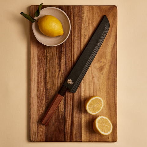 Bread knife in its wooden saya sheath on a cutting board with lemons