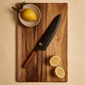 Gyuto knife in its wooden saya sheath on a cutting board with lemons